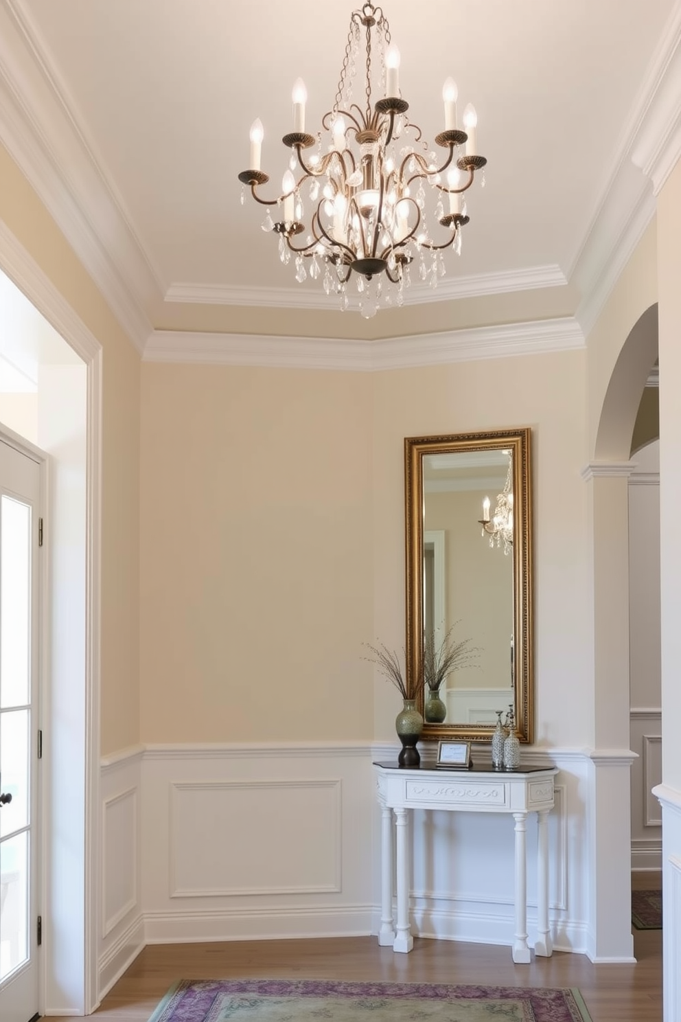 Classic white crown molding for sophistication. The foyer features elegant wainscoting and a stunning chandelier that draws the eye upward. The walls are painted in a soft neutral tone, creating a warm and inviting atmosphere. A console table adorned with decorative accents sits against one wall, complemented by a large mirror that enhances the sense of space.