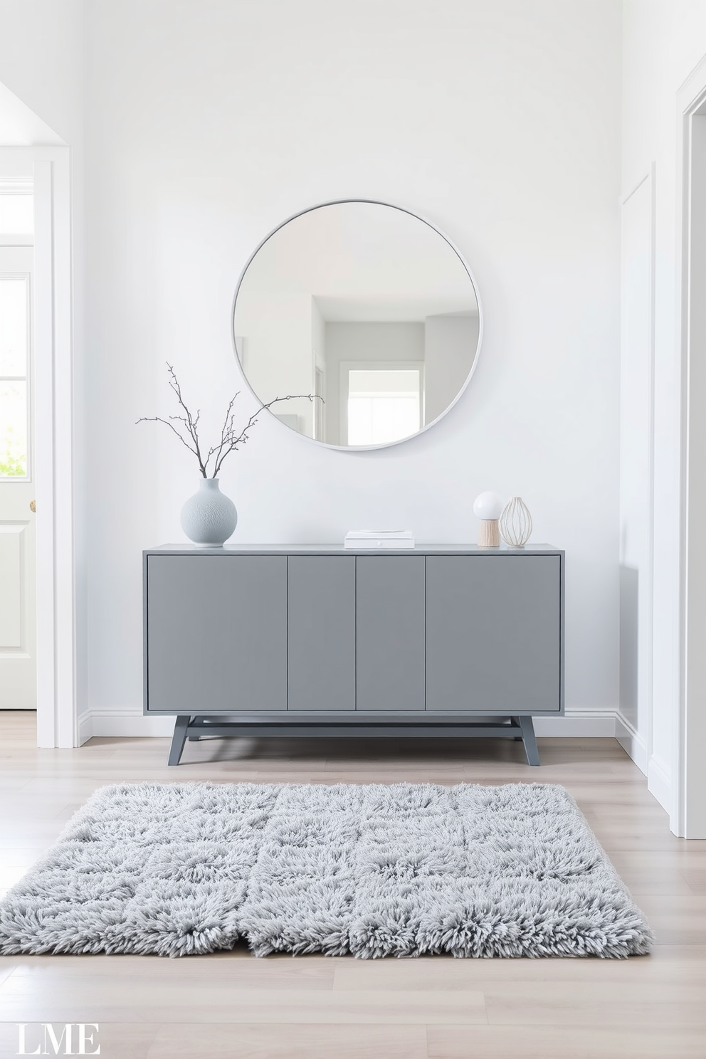 A serene foyer featuring a white and gray color palette that evokes calmness. The walls are painted a soft white, complemented by a sleek gray console table adorned with minimalist decor. A large round mirror with a simple white frame hangs above the console, reflecting natural light. A plush gray area rug lies beneath, adding warmth and comfort to the space.