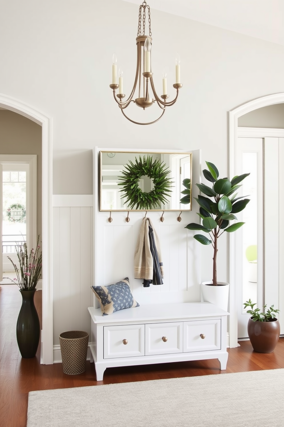 A white hall tree stands elegantly in the entryway, featuring hooks for coats and a bench for convenience. The backdrop is adorned with soft gray walls, and a stylish area rug adds warmth to the space. The foyer is designed with a bright and airy feel, showcasing a statement chandelier that illuminates the room. A large mirror above the hall tree enhances the sense of space, while potted plants bring a touch of nature indoors.