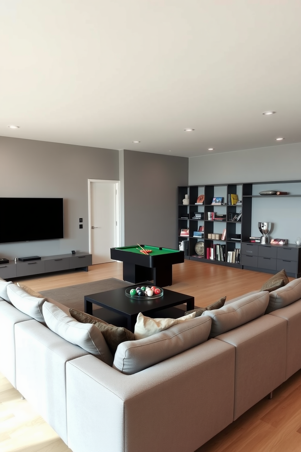 A modern game room features a sleek sectional sofa in a neutral color, positioned around a low-profile coffee table. The walls are painted in a soft gray, and a large flat-screen TV is mounted opposite the seating area. In one corner, a stylish pool table adds a touch of elegance, while minimalist shelving displays a curated selection of board games. The flooring is a light wood, creating a warm contrast with the contemporary furnishings.