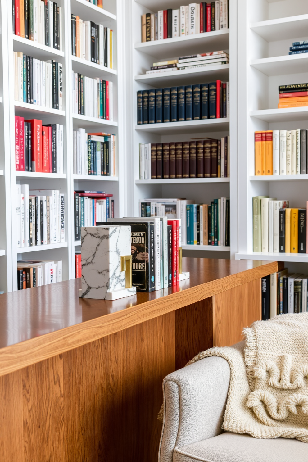 Unique bookends for personality and style. A pair of artistic bookends made from marble and brass stand proudly on a sleek wooden shelf, adding a touch of elegance to the collection of books. White home library design ideas. The room features floor-to-ceiling white bookshelves filled with books, complemented by a cozy reading nook with a plush armchair and a soft throw blanket.