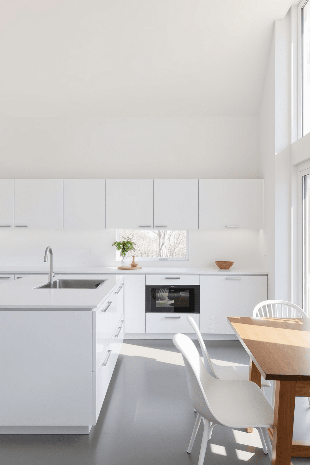 A minimalist kitchen featuring sleek white finishes. The cabinetry is handleless, creating a seamless look, and the countertops are made of polished white quartz. Natural light floods the space through large windows, highlighting the clean lines and open layout. A simple wooden dining table with white chairs complements the overall aesthetic.