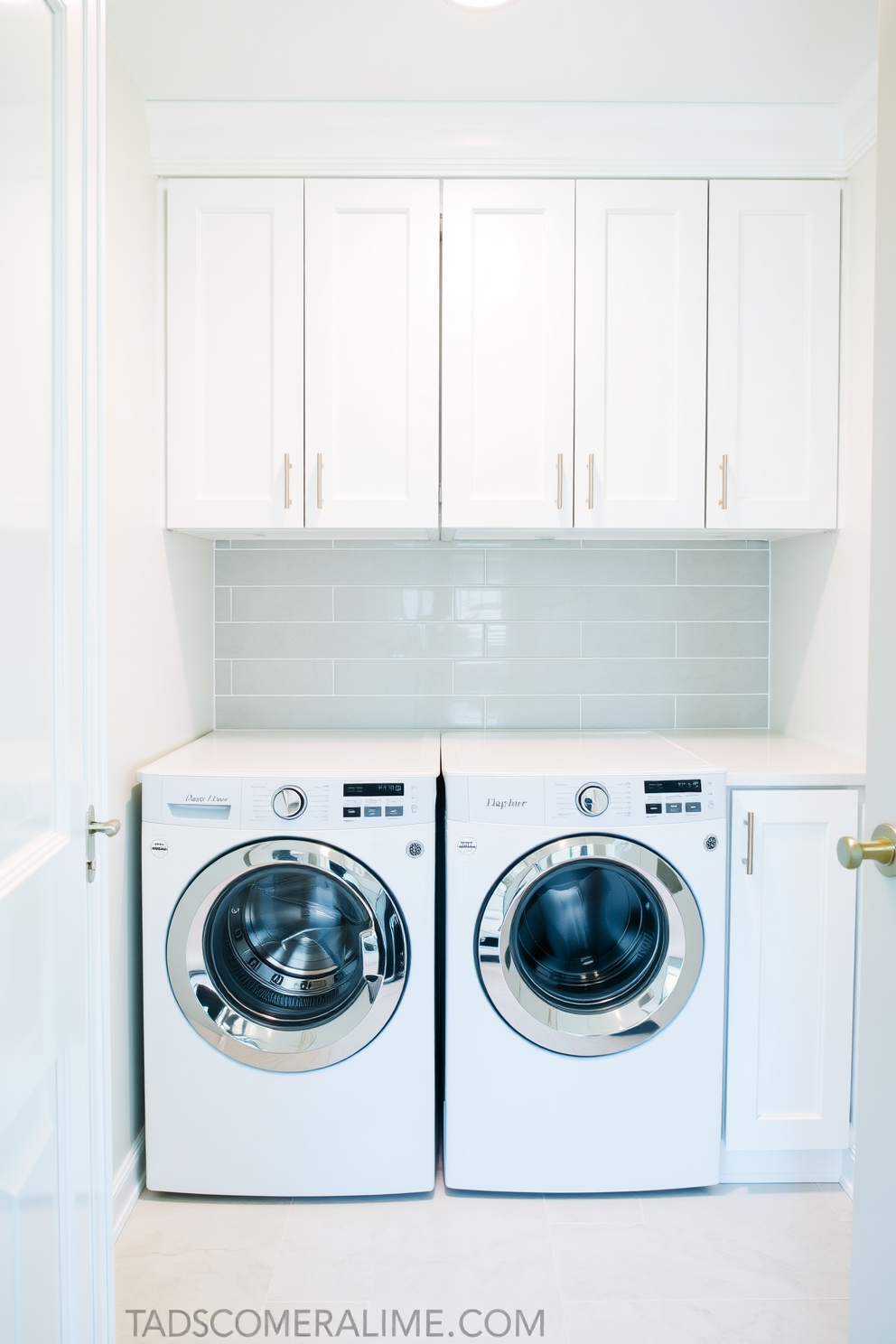 A bright and airy laundry room features a sleek design with a washer and dryer concealed behind elegant cabinet doors. The walls are painted in a soft white hue, complemented by a stylish backsplash of light gray tiles.