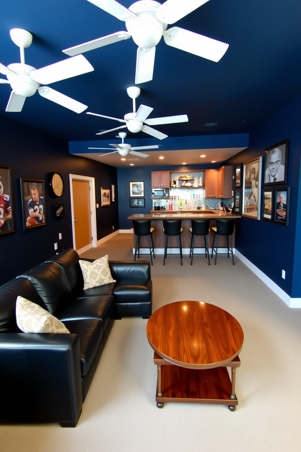 A stylish man cave featuring a comfortable sectional sofa in dark leather, positioned around a modern coffee table. The walls are painted in a deep navy blue, adorned with sports memorabilia and framed artwork that reflects personal interests. In the center of the room, a sleek bar area is equipped with high stools and a polished wooden countertop. White ceiling fans are installed for optimal airflow, adding both comfort and a contemporary touch to the space.