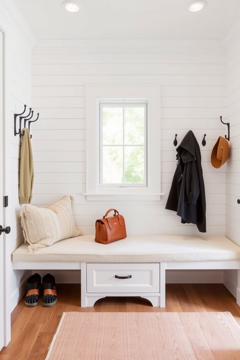 Bright white shiplap walls create a warm and inviting atmosphere in the mudroom. The space features built-in benches with plush cushions and hooks for hanging coats, providing both functionality and style.