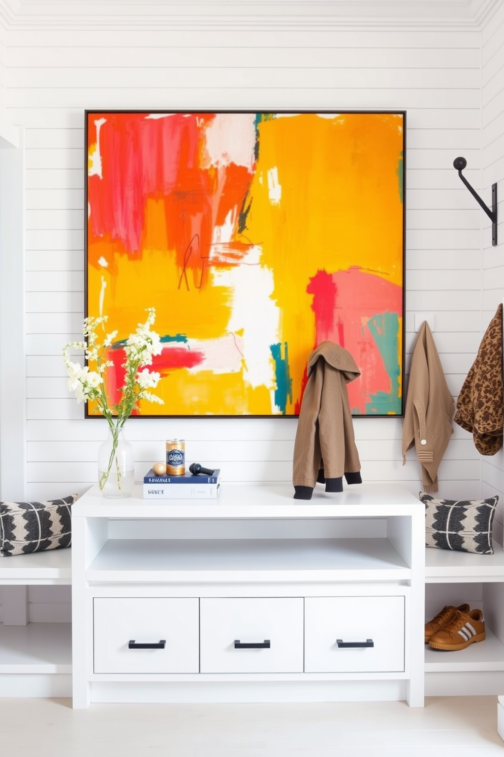 Stylish wall art for a personal touch. A large abstract painting in vibrant colors hangs above a sleek console table. White mudroom design ideas. The space features built-in benches with storage underneath and hooks for coats, all surrounded by shiplap walls painted in crisp white.