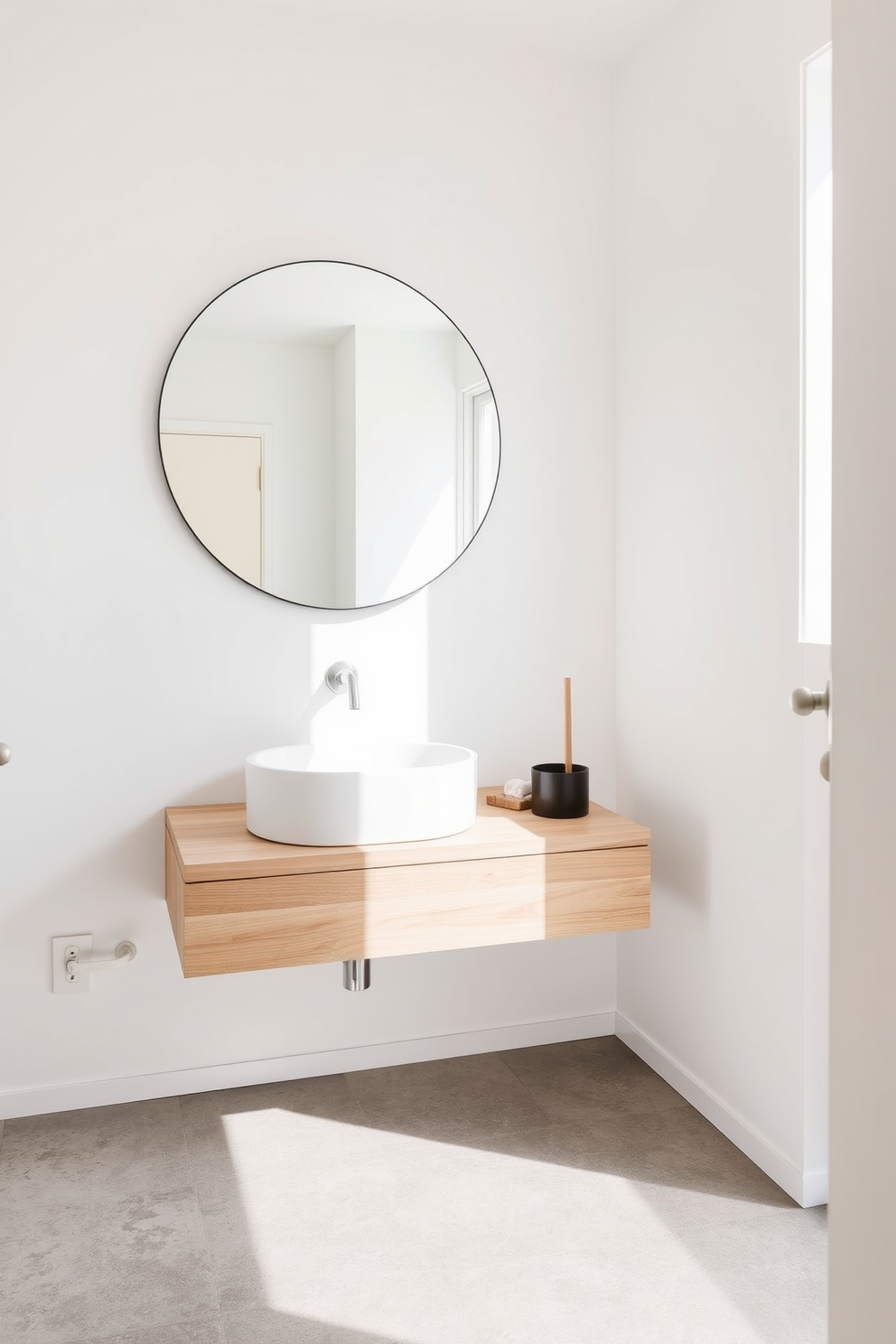 A minimalist powder room features a sleek floating vanity made of light wood with a simple white sink. The walls are painted in a soft white hue, creating an airy and open atmosphere. A large round mirror hangs above the vanity, reflecting natural light that floods in from a nearby window. The floor is adorned with large concrete tiles, enhancing the modern aesthetic of the space.