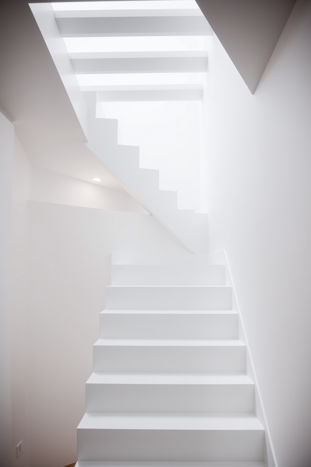 A Scandinavian white staircase featuring clean lines and a minimalist design. Soft recessed lighting highlights the staircase, creating a warm and inviting atmosphere.