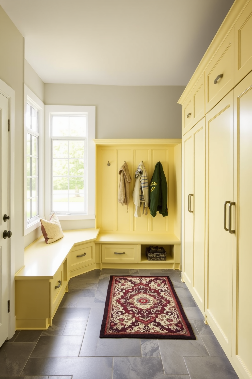 A bright and inviting mudroom features light yellow cabinetry that adds a fresh and cheerful touch to the space. The cabinetry is complemented by a durable gray tile floor and a large window that allows natural light to flood in. Functional storage solutions include built-in benches and hooks for coats, creating an organized and welcoming entryway. A decorative rug in soft neutrals ties the room together, enhancing the overall cozy atmosphere.