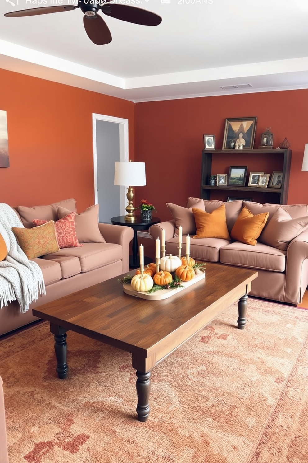 A cozy fall living room setting. There are plush sofas adorned with warm-toned throw pillows and a soft knitted blanket draped over one armrest. A wooden coffee table sits at the center, decorated with a rustic centerpiece of pumpkins and candles. The walls are painted in a rich burnt orange, and a large area rug in earthy tones anchors the space. Gold accents are incorporated through picture frames and decorative objects on the shelves. Warm, ambient lighting from stylish floor lamps creates an inviting atmosphere perfect for fall gatherings.