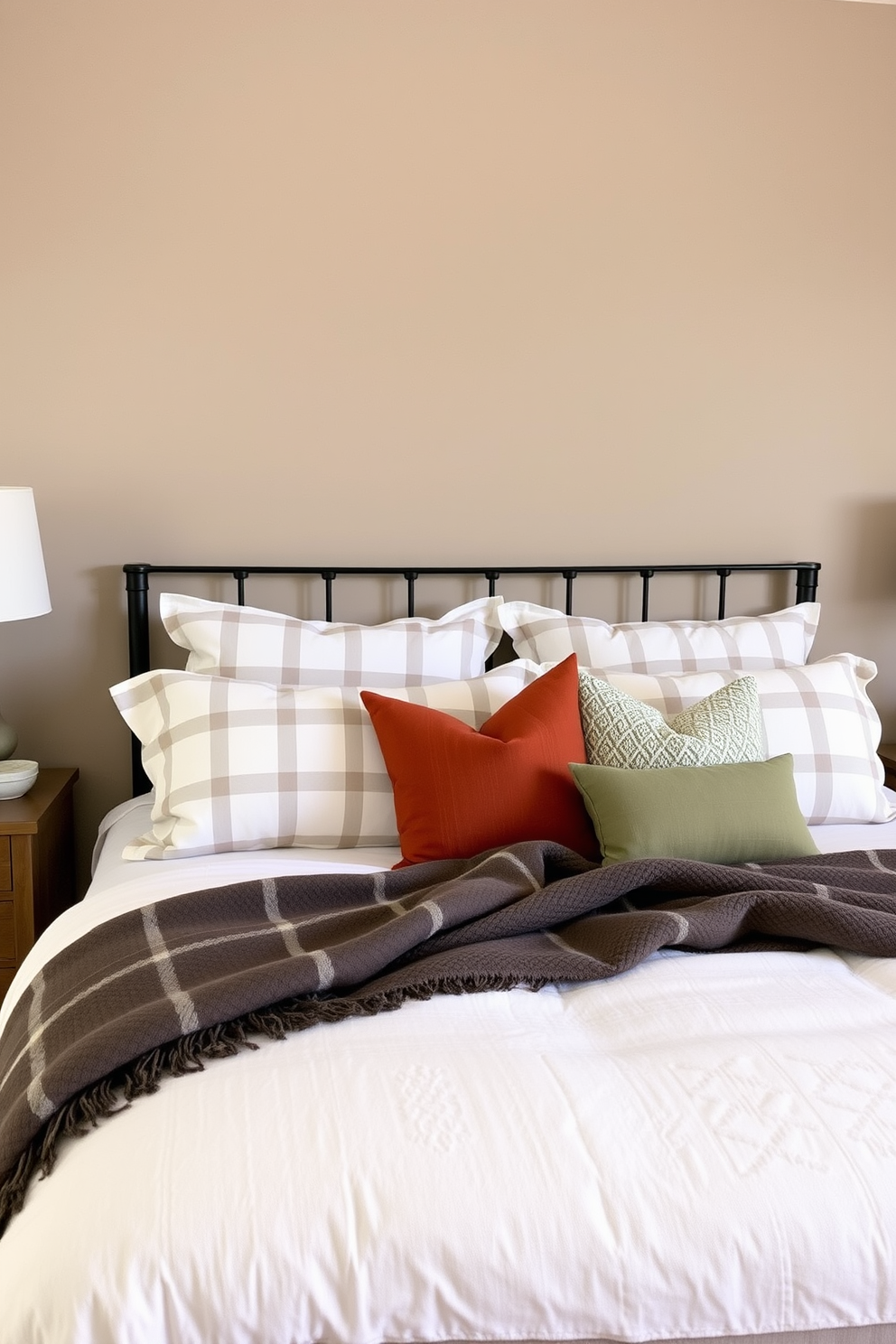 A cozy fall bedroom setting with soft, muted colors that evoke a sense of warmth and tranquility. The walls are painted in a gentle taupe, and the bedding features a subtle plaid pattern in shades of cream and soft brown. A plush throw blanket is draped over the foot of the bed, adding texture and comfort. Decorative pillows in muted rust and sage green are arranged artfully on the bed to enhance the seasonal theme.