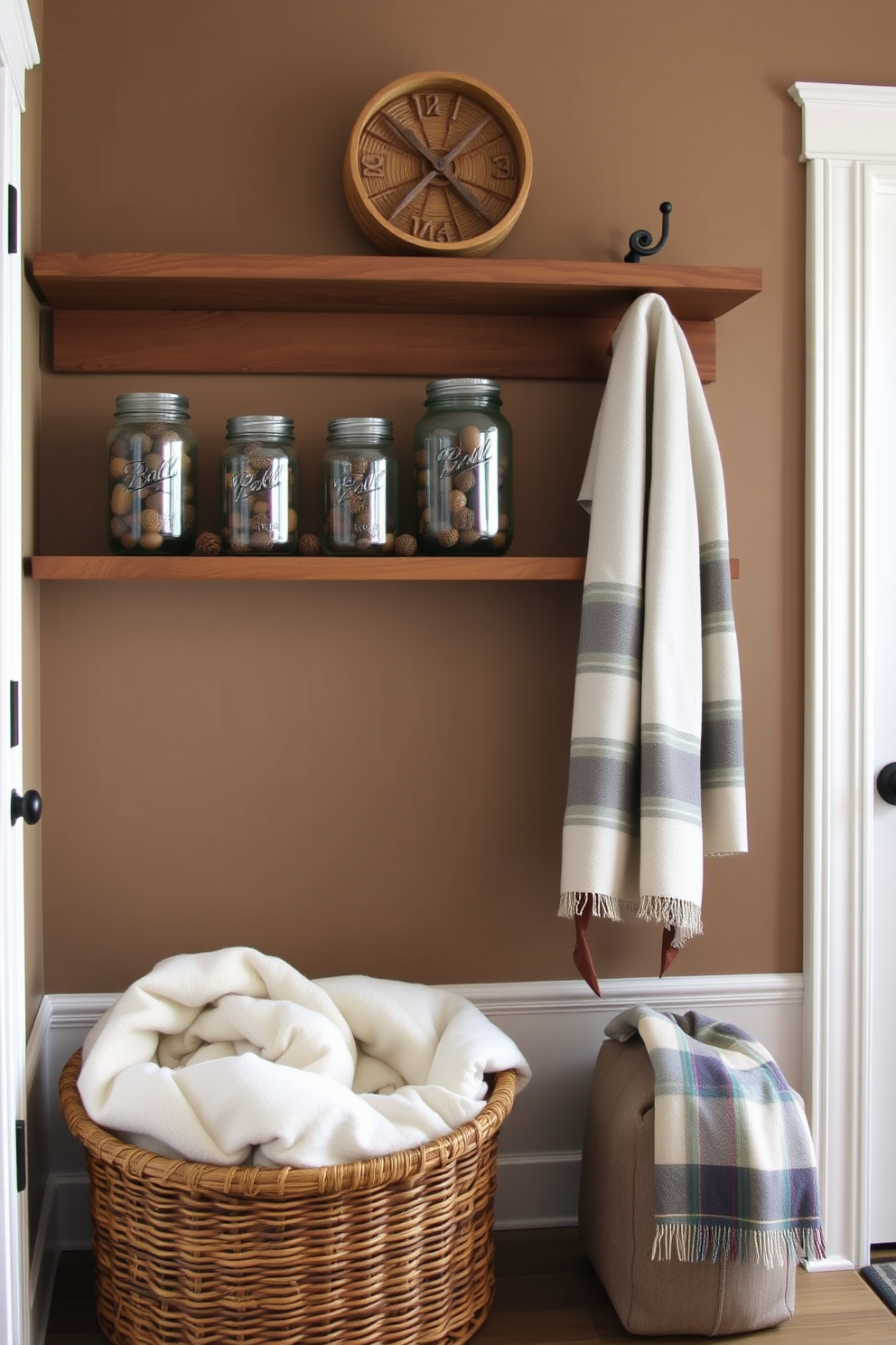 A cozy mudroom features rustic charm with mason jars filled with acorns and pinecones displayed on a wooden shelf. The walls are painted in a warm taupe, and a woven basket sits on the floor, holding extra blankets for chilly days.