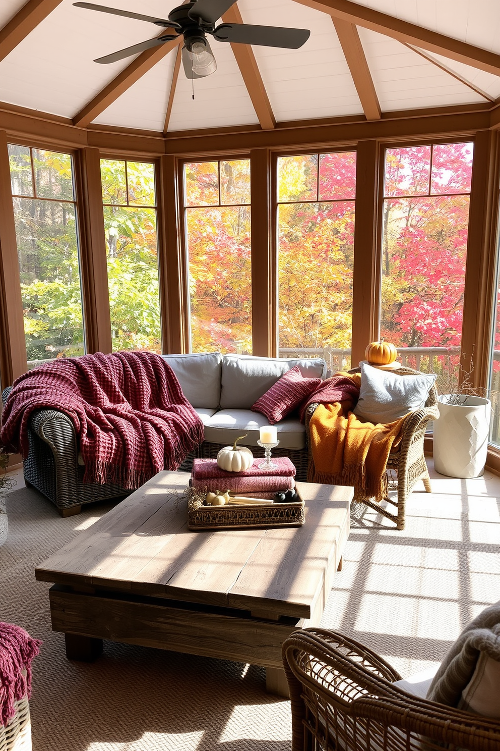 A cozy sunroom filled with natural light. Textured throws in warm autumn colors are draped over a plush sofa and a wicker chair, creating an inviting atmosphere. The walls are adorned with large windows that showcase the vibrant fall foliage outside. A rustic wooden coffee table sits in the center, topped with a collection of seasonal decor and a stack of cozy blankets.