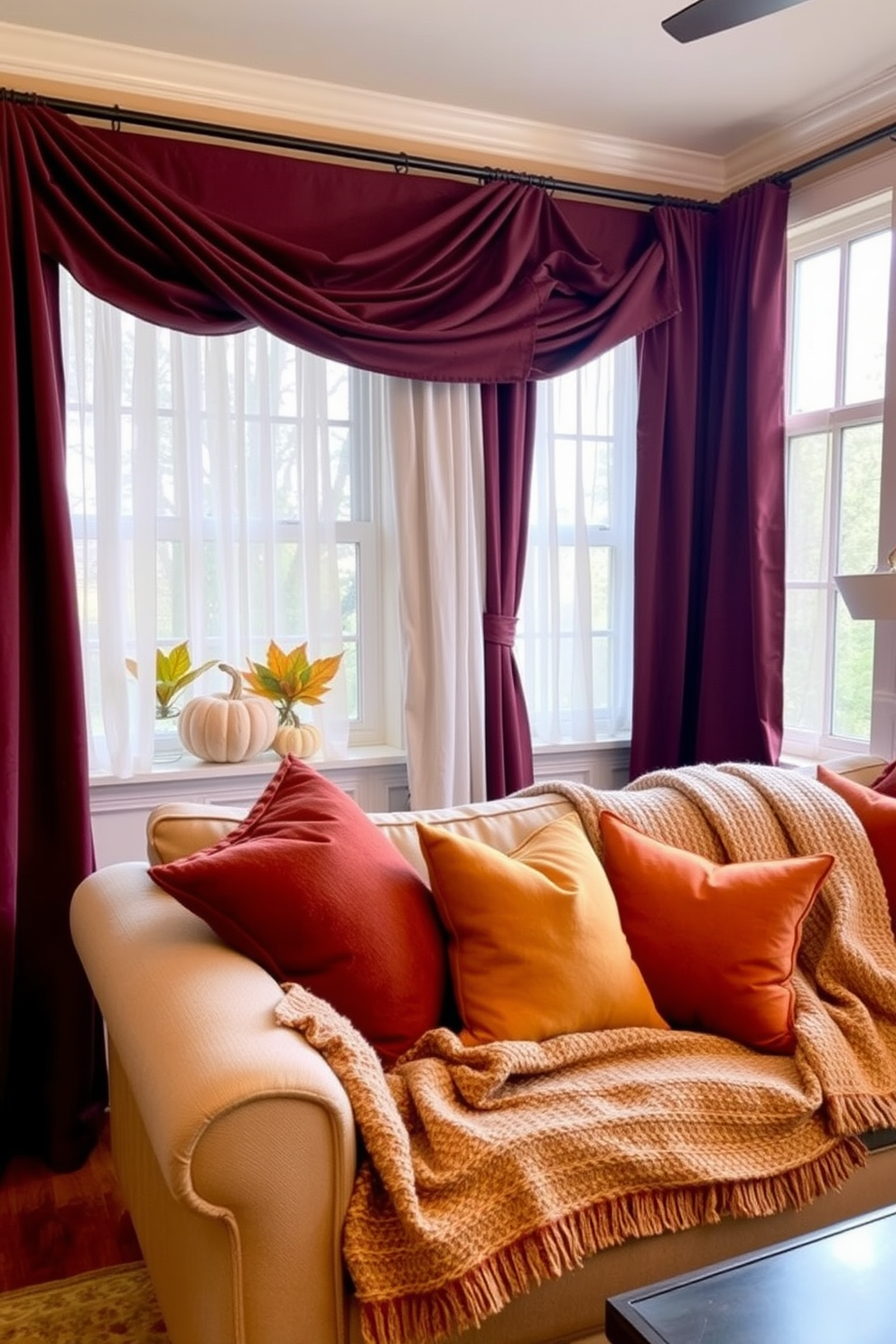 A warm and inviting living room features layered fabrics that create a cozy texture. Plush throw pillows in rich autumn colors are scattered across a soft, oversized sofa draped with a knitted blanket. The windows are adorned with sheer curtains that gently diffuse the natural light, complemented by heavier drapes in deep burgundy. Seasonal decorations, such as small pumpkins and colorful leaves, are placed on the window sill to enhance the fall ambiance.