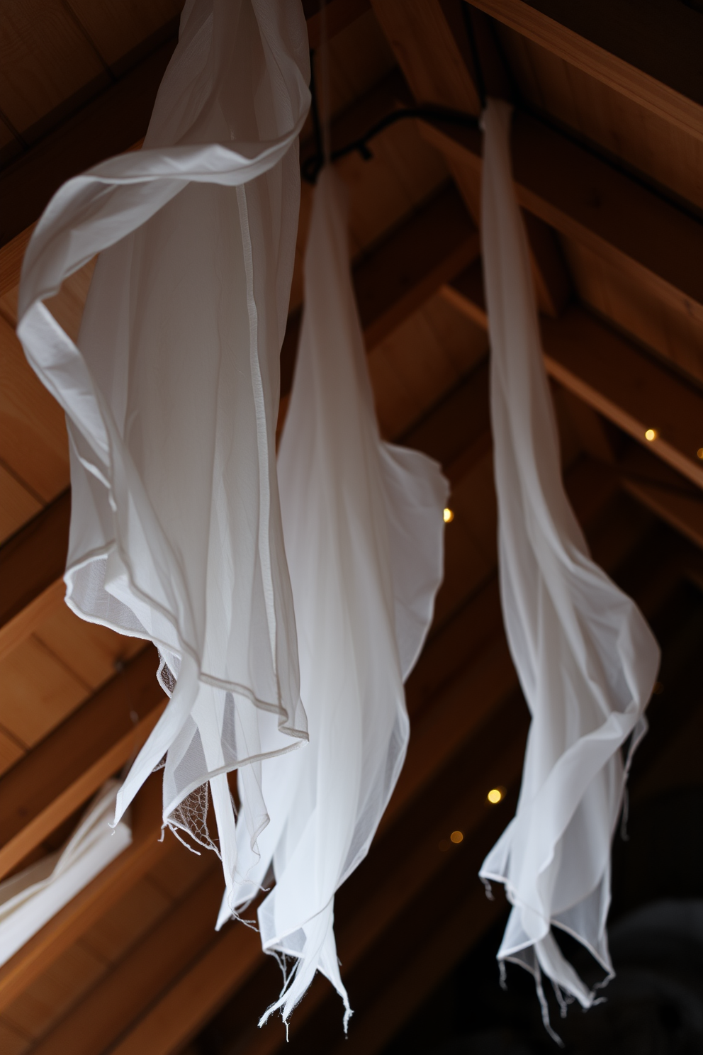 Hanging fabric ghosts drift gently from the rafters, creating an eerie yet whimsical atmosphere in the attic. Soft white and gray fabrics billow in the breeze, illuminated by dim, flickering lights that enhance the Halloween spirit.