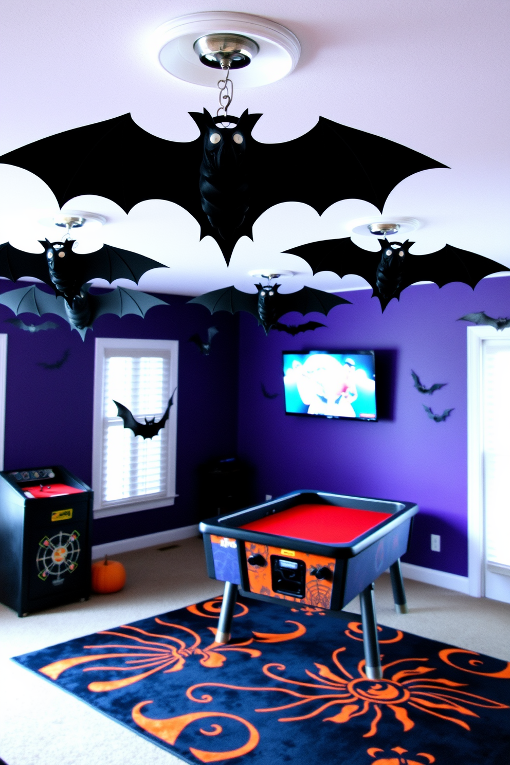 A Halloween-themed game room features hanging bats from ceiling fixtures that create an eerie atmosphere. The walls are painted in deep purple, and the floor is adorned with a black and orange area rug, enhancing the festive spirit.