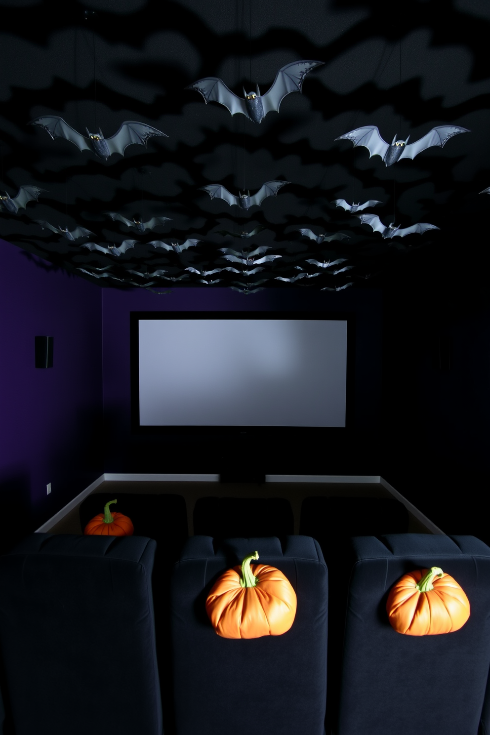 A spooky home theater setting for Halloween. The ceiling is adorned with hanging bats made of black paper, casting eerie shadows across the room. The walls are painted a deep purple, creating a dramatic backdrop. Plush black seating is arranged in front of a large screen, with pumpkin-shaped pillows adding a festive touch.