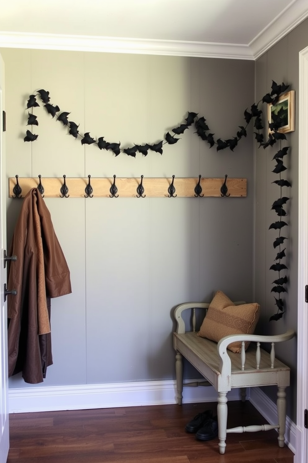 A cozy mudroom adorned with bat garlands draped elegantly across rustic hooks. The walls are painted in a warm gray tone, and a vintage bench sits against one side, inviting guests to sit and remove their shoes.