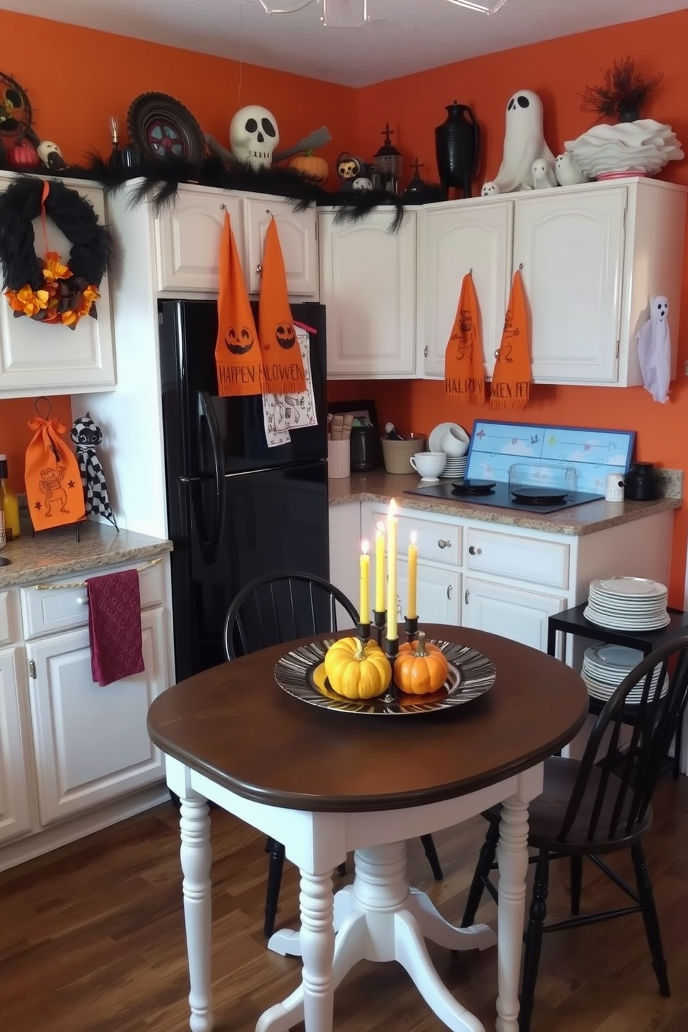 A cozy kitchen setting designed for Halloween. The space features a small dining table adorned with festive decorations and a centerpiece of pumpkins and candles. On the countertops, there are vibrant Halloween-themed dish towels hanging next to a collection of spooky dishware. The walls are painted in warm autumn hues, and a few ghostly decorations are placed throughout the space to enhance the festive atmosphere.