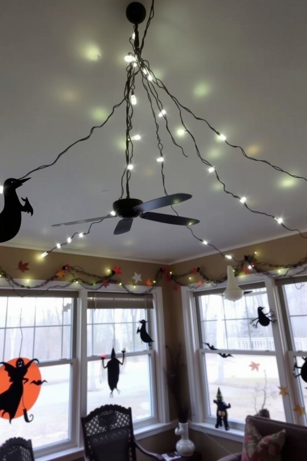 Spooky string lights are draped across the ceiling of a sunroom, casting an eerie glow throughout the space. The walls are adorned with Halloween-themed decorations, including ghostly silhouettes and autumn leaves, creating a festive atmosphere.