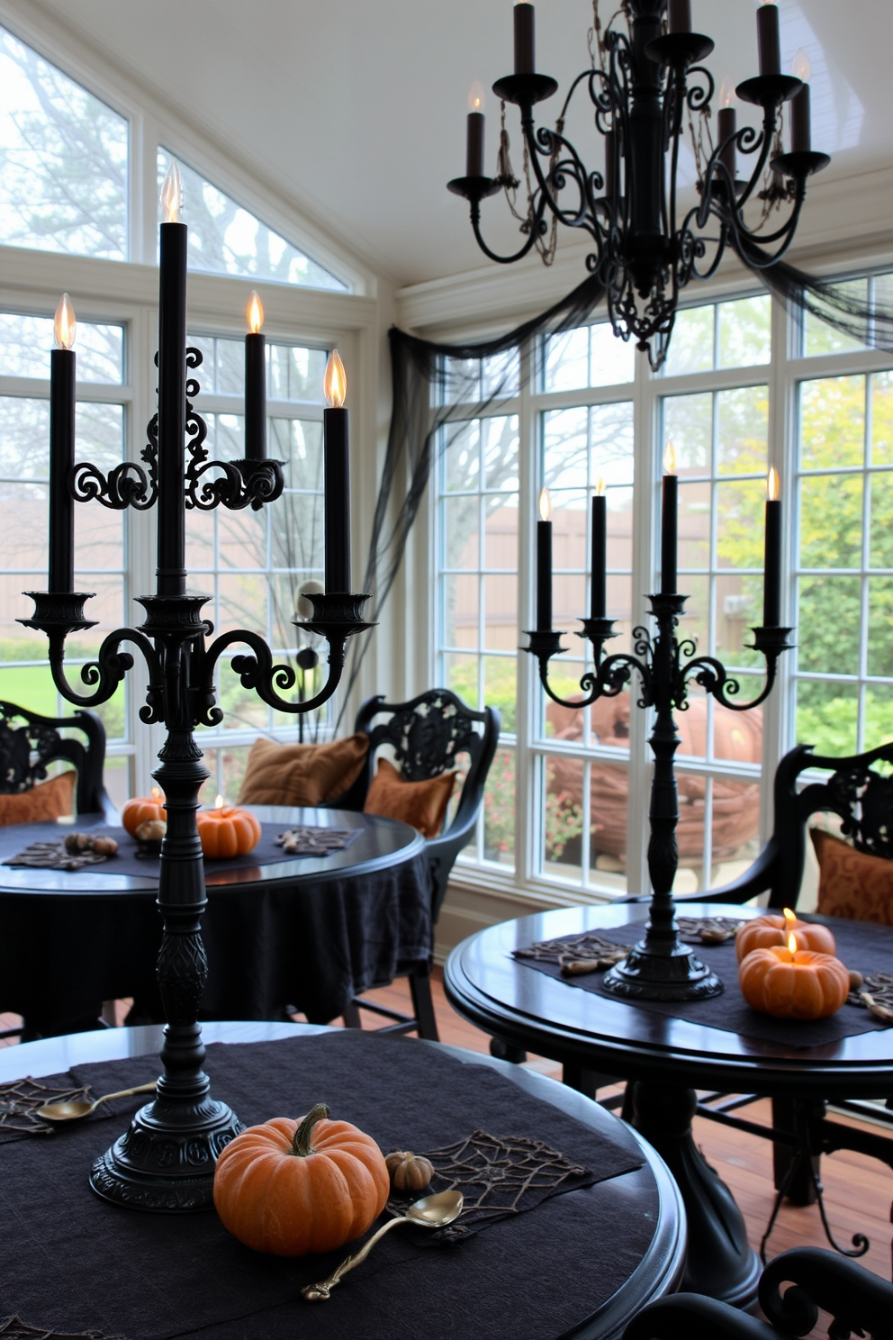 A sunroom decorated for Halloween features elegant tables adorned with ornate candelabras holding black candles. The ambiance is enhanced by autumnal decor, including pumpkins and rich, warm textiles that invite a cozy atmosphere.