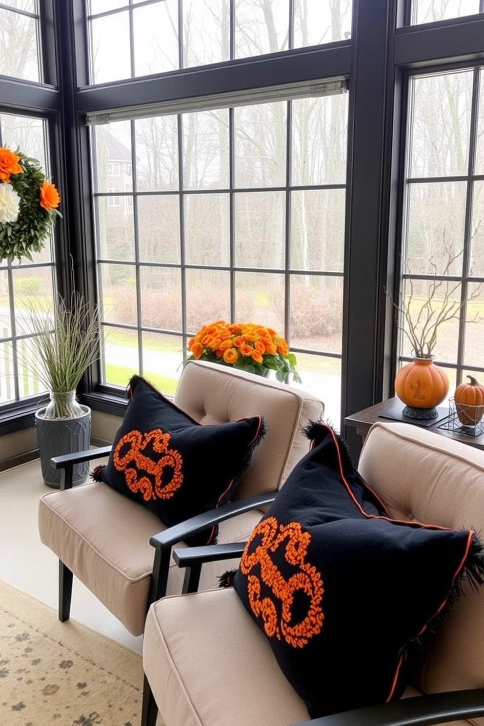 Black and orange throw pillows are placed on comfortable chairs in a sunroom, adding a festive touch for Halloween. The sunroom features large windows that let in natural light, showcasing a cozy atmosphere with seasonal decorations.