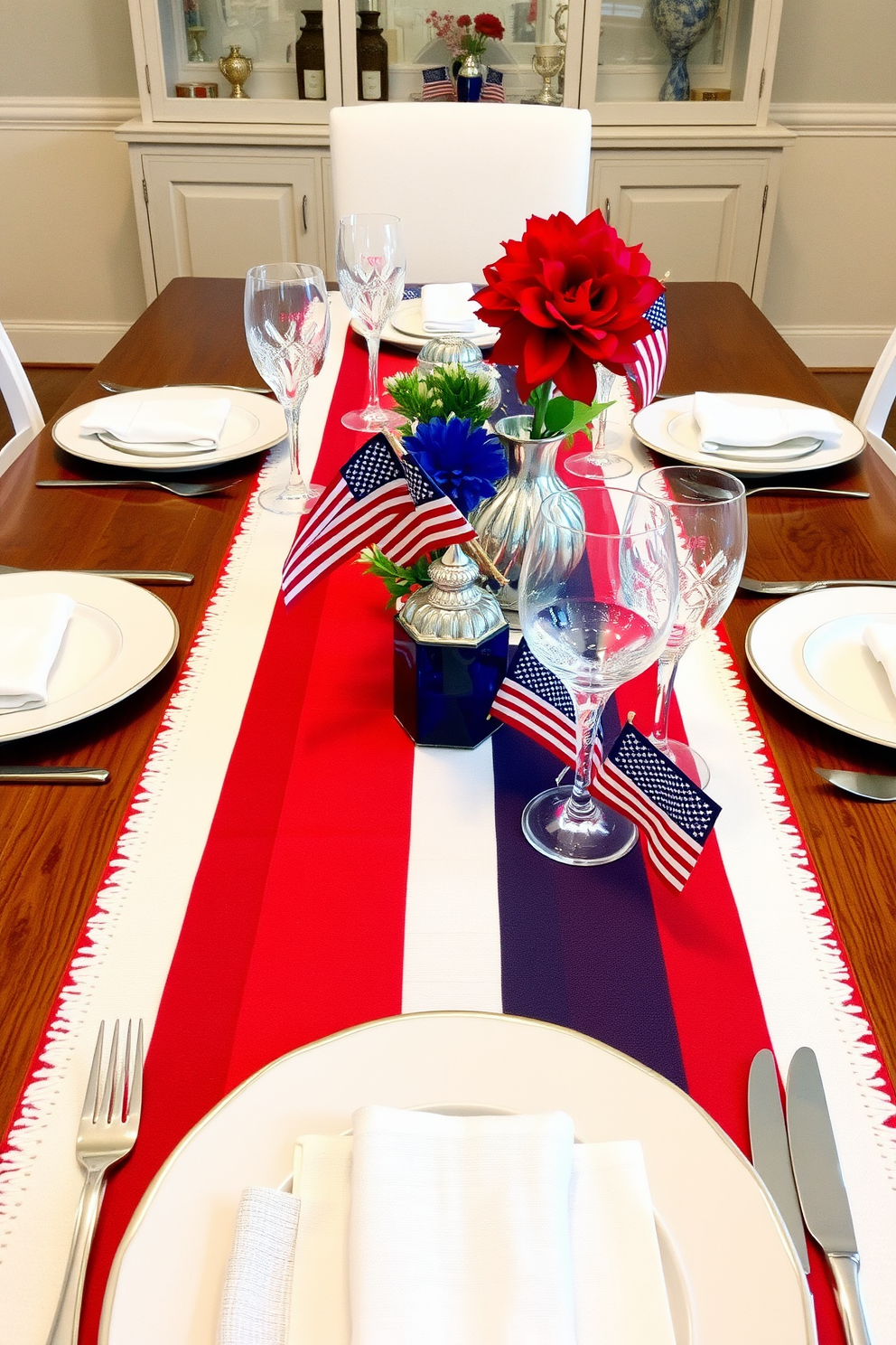 A festive dining table adorned with a red white and blue table runner that captures the spirit of Independence Day. Surrounding the table are elegant white plates and sparkling glassware, complemented by small American flag centerpieces.