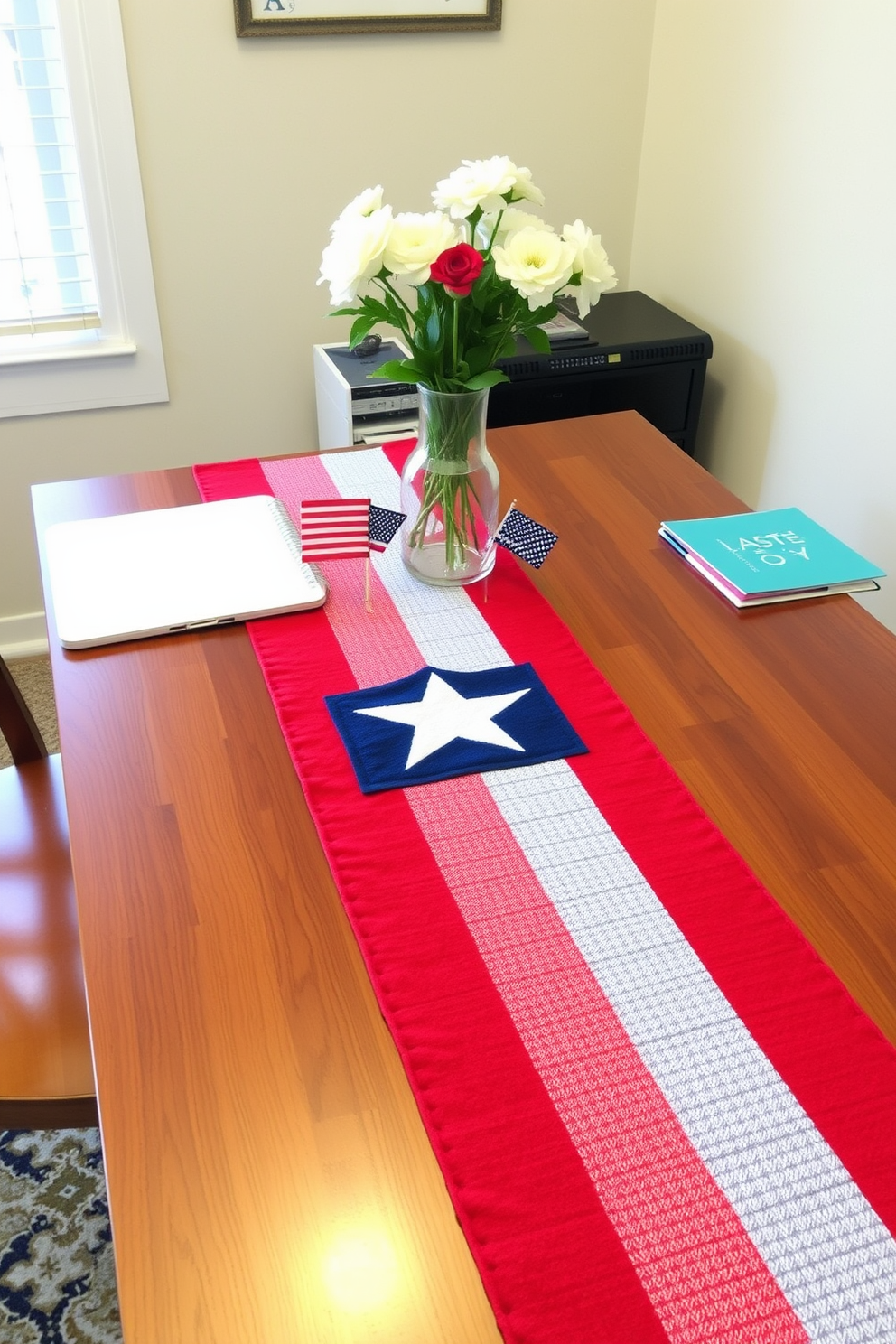 A patriotic table runner adorns the workspace, featuring red, white, and blue stripes that celebrate Independence Day. The runner adds a festive touch to the home office, complemented by small decorative flags and a vase of fresh flowers.