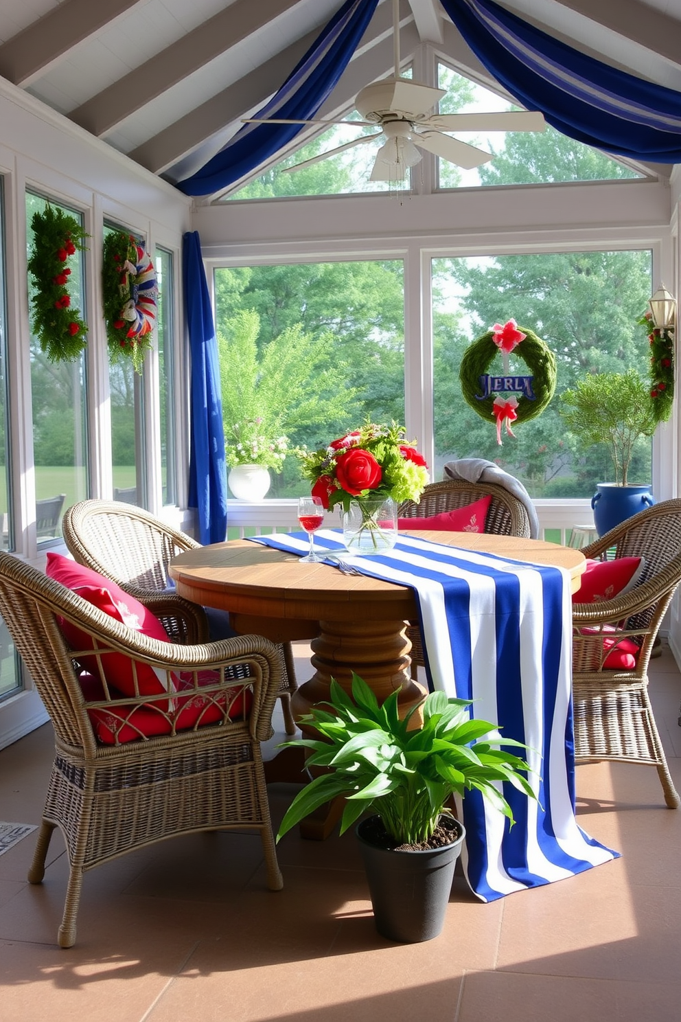 A sunroom decorated for Independence Day features a blue and white striped tablecloth elegantly draped over a rustic wooden table. Surrounding the table are comfortable wicker chairs adorned with red cushions, creating a festive and inviting atmosphere.