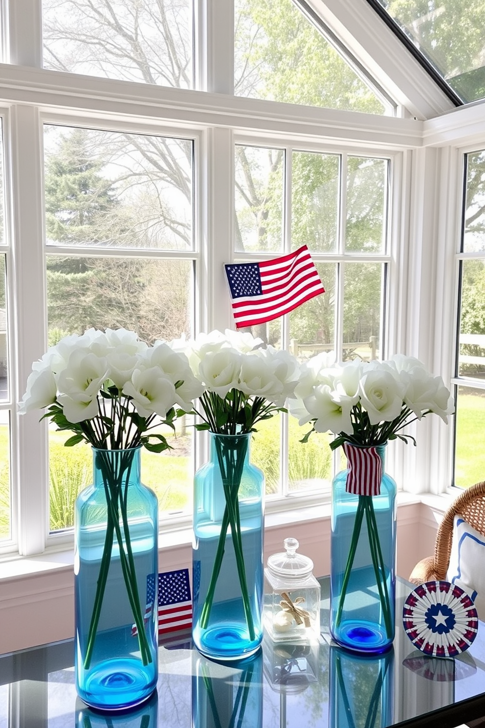 A sunroom filled with natural light features blue glass vases elegantly arranged with fresh white flowers. The decor incorporates red, white, and blue accents to celebrate Independence Day, creating a festive and inviting atmosphere.