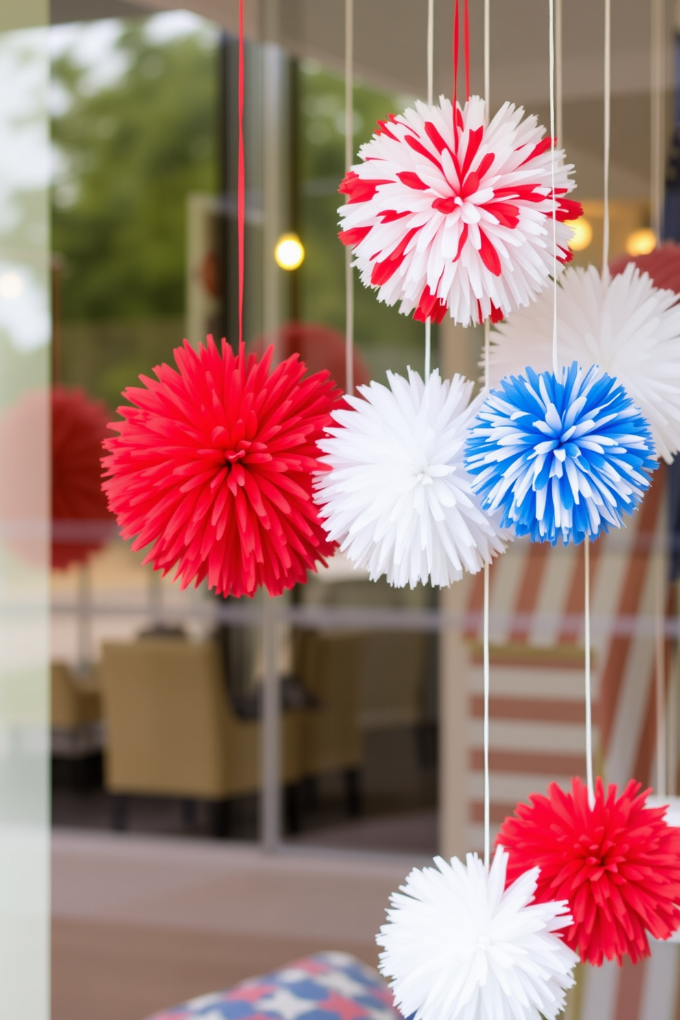 Create a festive window display for Independence Day featuring hanging red white and blue pom poms. The pom poms should be arranged in a playful manner, creating a vibrant and celebratory atmosphere that captures the spirit of the holiday.