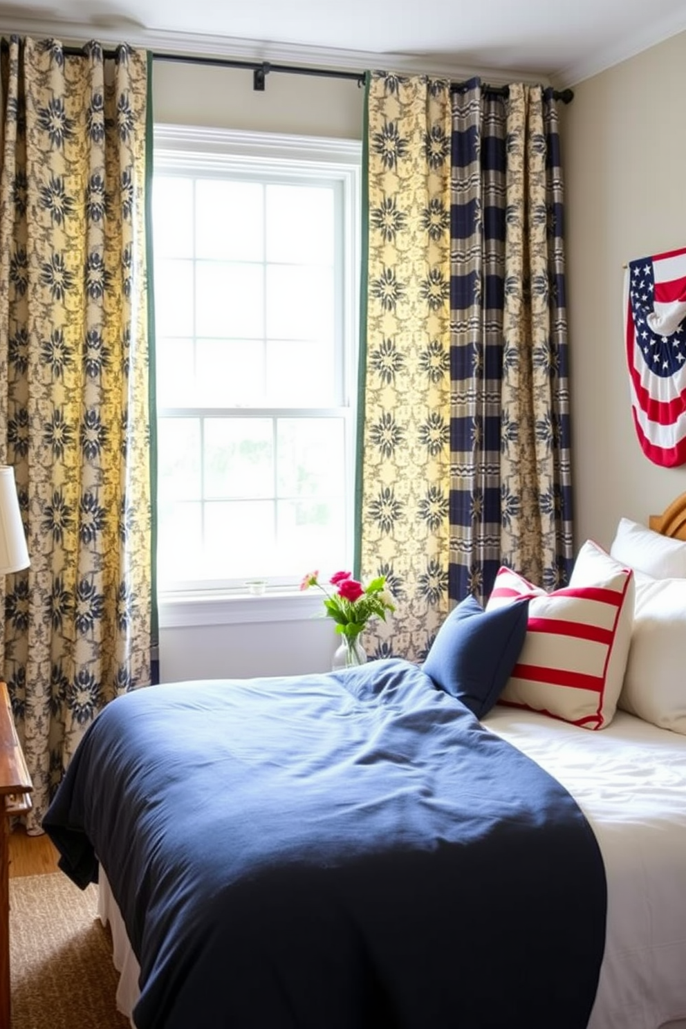 A cozy bedroom designed for Labor Day celebration. The room features patterned curtains that add visual interest, framing a large window that lets in natural light. A plush bed with a soft, navy blue duvet sits center stage, complemented by decorative pillows in red and white. A rustic wooden nightstand holds a small vase of fresh flowers, enhancing the inviting atmosphere.