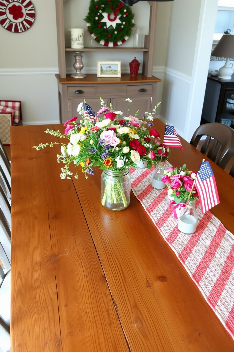 A rustic farmhouse table setting features a large wooden table with a weathered finish surrounded by mismatched chairs. Centered on the table, a bouquet of wildflowers is arranged in a vintage mason jar, adding a touch of charm. For Labor Day dining room decorating ideas, the space is adorned with red, white, and blue accents throughout. A festive table runner complements the seasonal decor, while small American flags are placed in each floral arrangement.