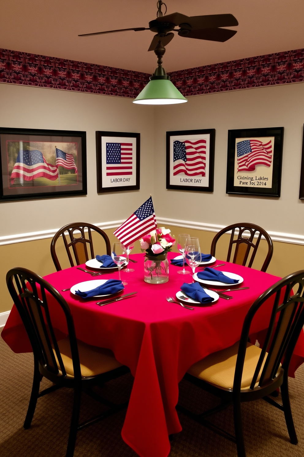 A patriotic dining room setting features a table set with a vibrant red tablecloth and white dinnerware accented with blue napkins. The walls are adorned with framed artwork that showcases American flags and Labor Day themes, creating a festive atmosphere.