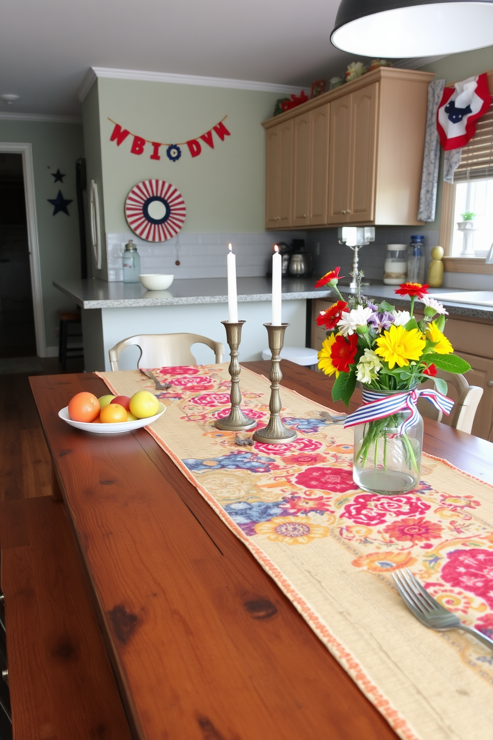 A vibrant table runner stretches across a rustic wooden dining table set for a festive gathering. The runner features a lively pattern of red, blue, and yellow hues, complemented by an array of seasonal fruits and candles that enhance the celebratory atmosphere. The kitchen is adorned with cheerful decorations, incorporating red, white, and blue accents to honor Labor Day. Fresh flowers in a mason jar sit on the countertop, while playful banners and artwork add a touch of whimsy to the space.