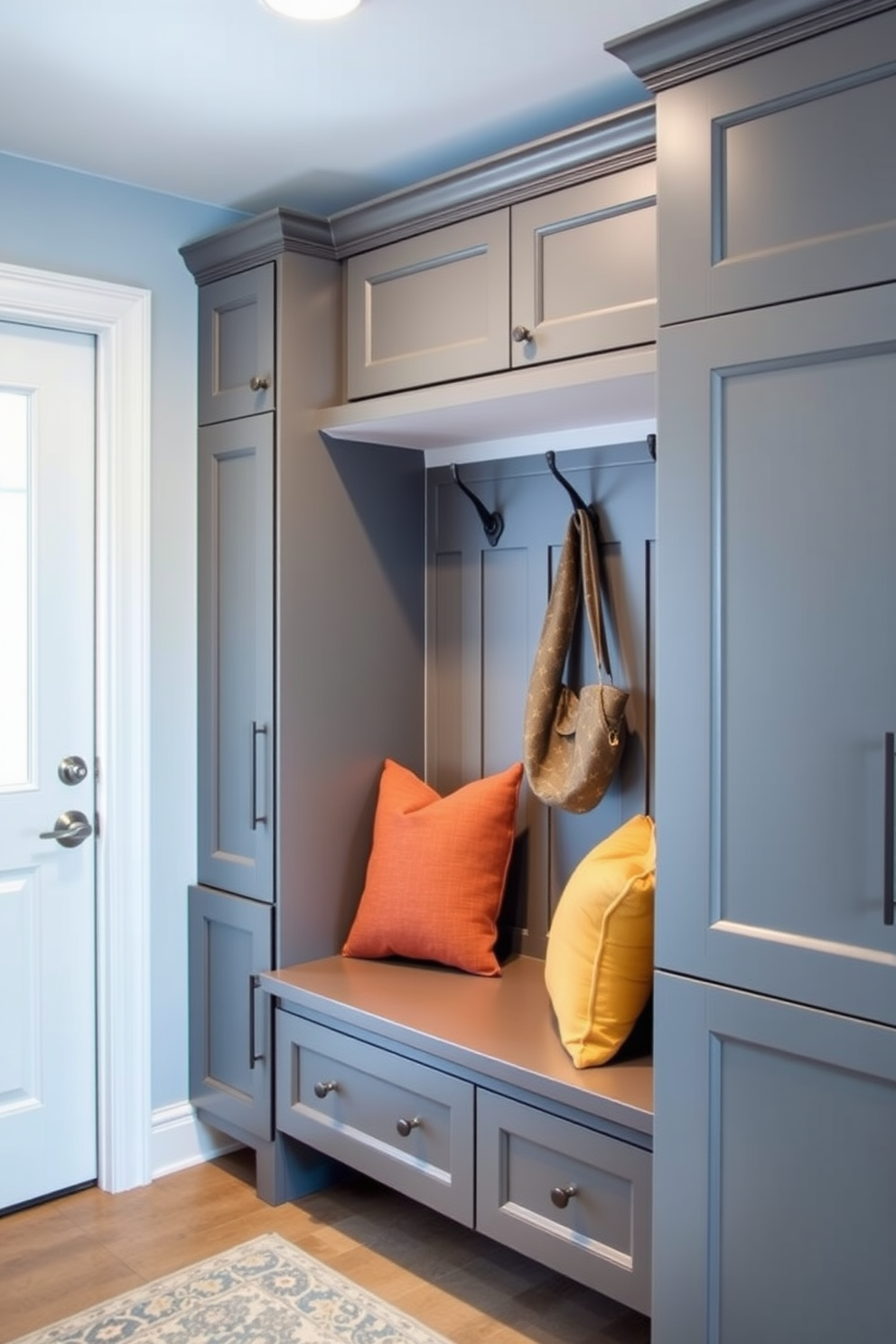 A welcoming mudroom that features a coordinated color scheme of soft blues and warm grays. The walls are painted in a light blue shade, while the cabinetry showcases a deep gray finish for a balanced look. Stylish hooks and storage solutions are arranged neatly along one wall, providing functional yet decorative elements. A cozy bench with plush cushions in complementary colors invites relaxation and organization.