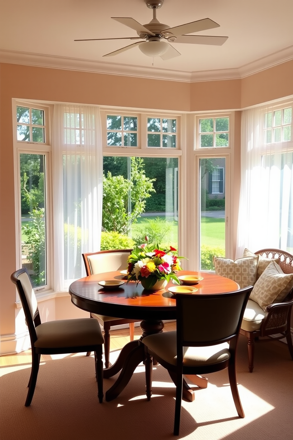 A sun-drenched breakfast area features a round wooden table surrounded by comfortable upholstered chairs. Large windows allow natural light to flood the space, with sheer white curtains gently framing the view of a lush garden. The walls are painted in a soft pastel hue, creating a warm and inviting atmosphere. A vibrant centerpiece of fresh flowers sits on the table, complemented by a cozy nook with plush cushions in the corner.