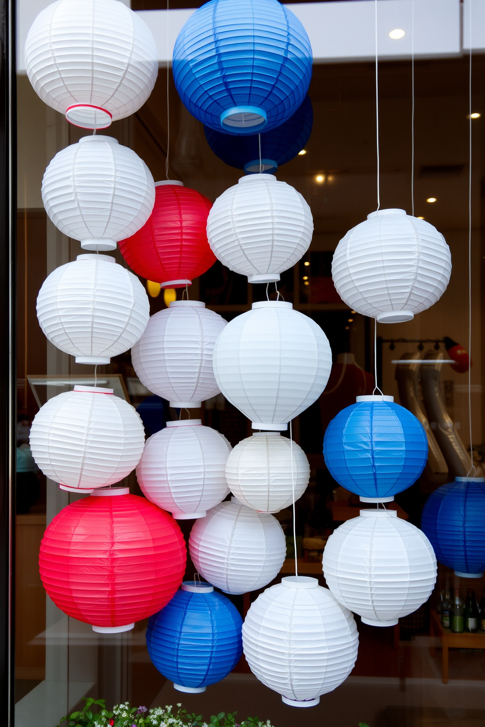 A festive window display featuring paper lanterns in red white and blue. The lanterns are hung at varying heights, creating a playful and patriotic atmosphere.