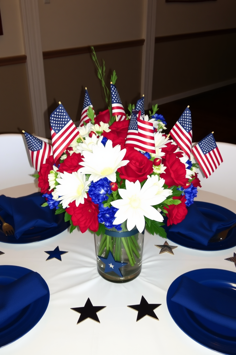 A festive table centerpiece featuring a mix of red white and blue flowers arranged in a glass vase. Small American flags are inserted among the blooms creating a patriotic display perfect for Memorial Day celebrations. The table is set with a white tablecloth and blue dinnerware adding to the festive atmosphere. Decorative stars and stripes accents are placed around the centerpiece enhancing the overall theme of remembrance and celebration.