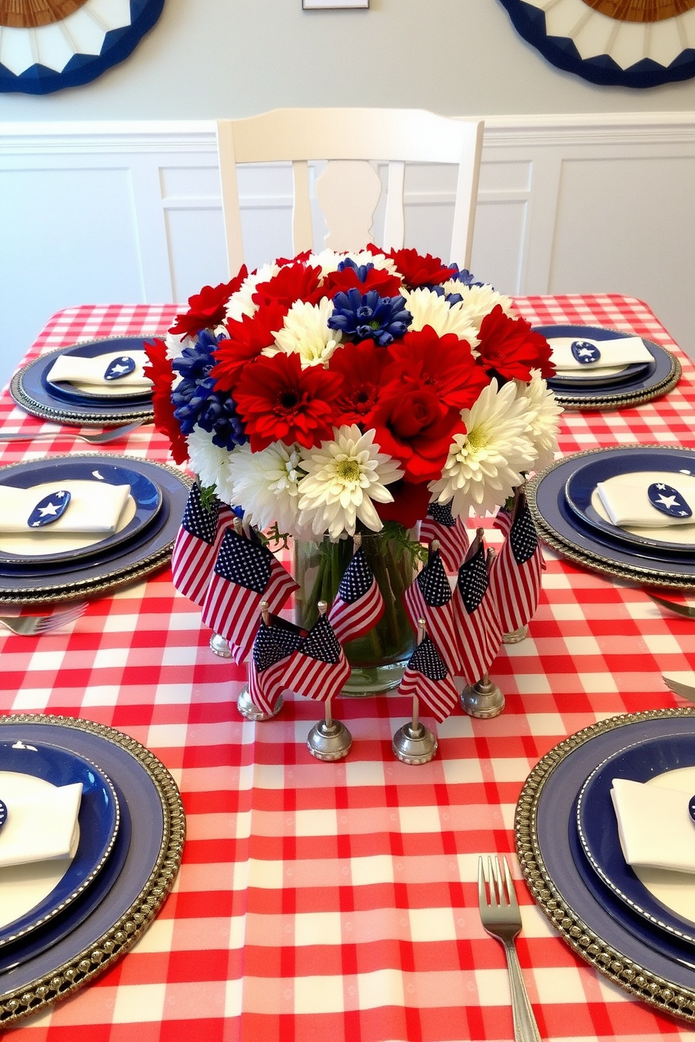 A festive table setting for Memorial Day featuring a red and white checkered tablecloth topped with blue and white dinnerware. The centerpiece includes a bouquet of red, white, and blue flowers in a glass vase surrounded by small American flags.