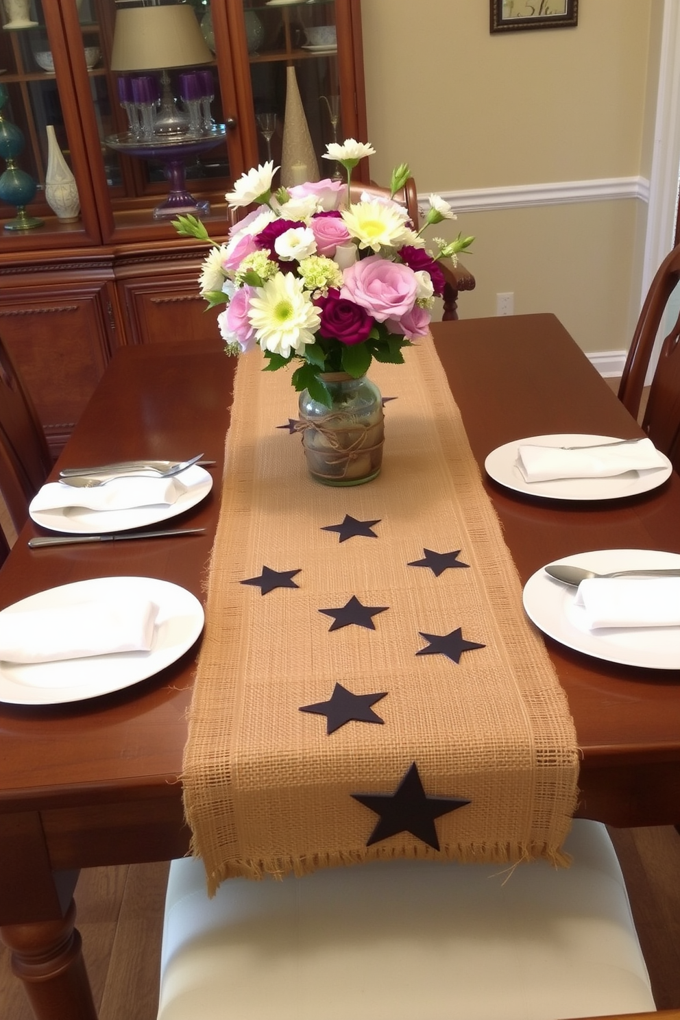 A beautifully set dining table features a burlap table runner adorned with star embellishments. The table is surrounded by elegant wooden chairs, and a centerpiece of fresh flowers in a rustic vase adds a touch of charm.