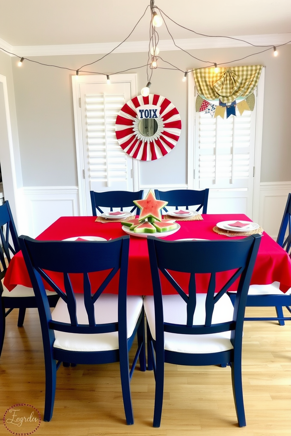 A festive dining room setting for Memorial Day. The table is adorned with a vibrant red tablecloth and white plates featuring star-shaped watermelon slices as a centerpiece. Surrounding the table are navy blue chairs with white cushions. String lights hang overhead, adding a warm glow to the celebration atmosphere.