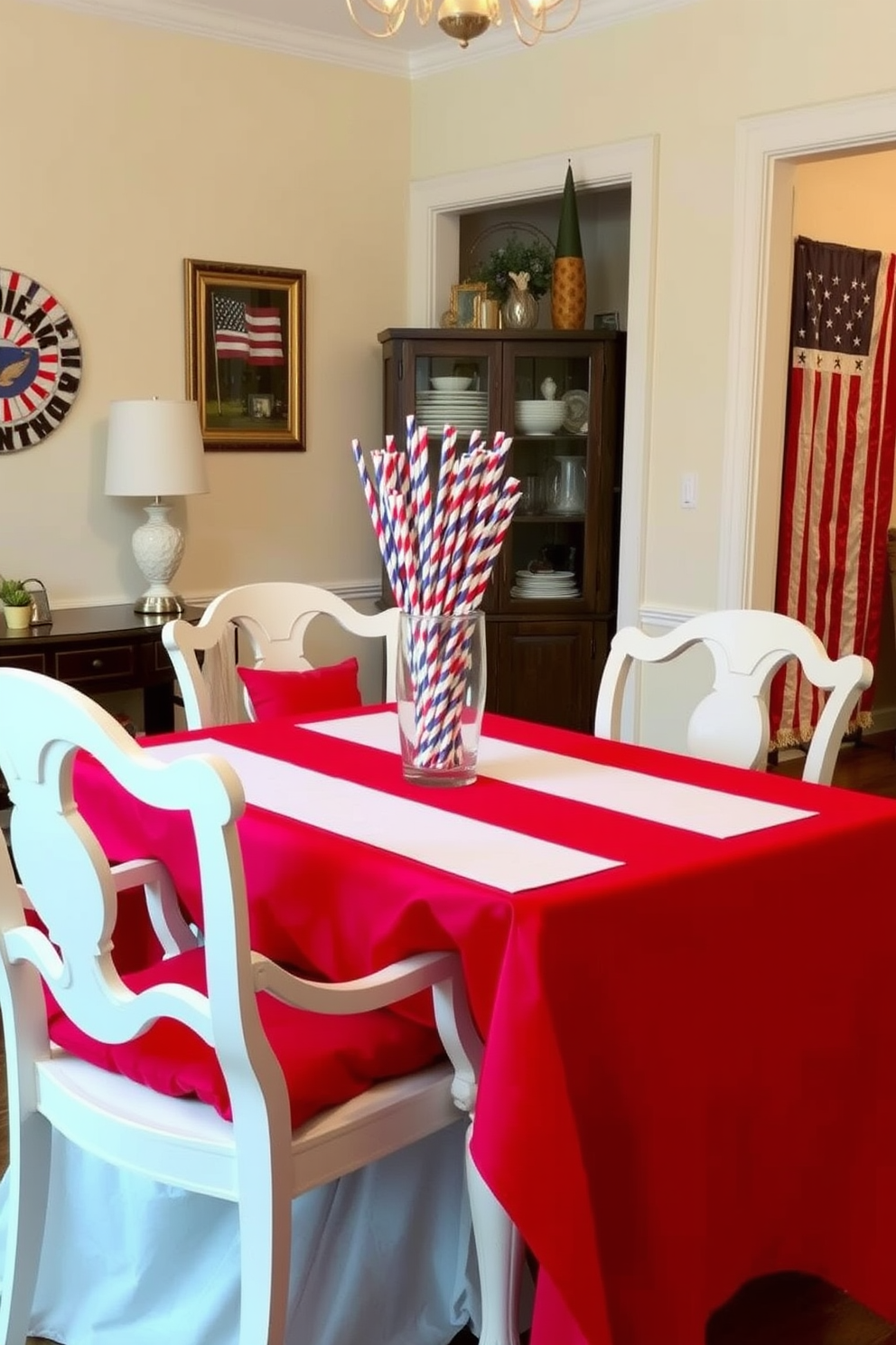 A festive dining room setting for Memorial Day featuring a table adorned with a vibrant red tablecloth. On the table, there are red blue and white striped straws in a clear glass vase, adding a playful touch to the decor. Surrounding the table are elegant white chairs with red cushions, creating a cohesive color scheme. The walls are decorated with patriotic-themed artwork, enhancing the celebratory atmosphere of the room.