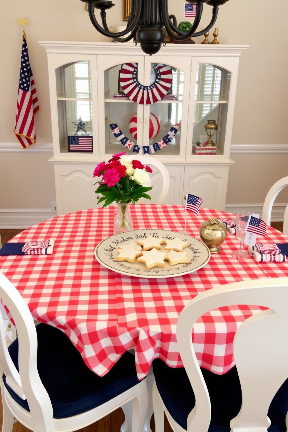 A charming dining room setting for Memorial Day featuring a beautifully arranged table. The table is adorned with a red and white checkered tablecloth, and star shaped cookies are artfully displayed on a decorative platter at the center. Surrounding the table are elegant white chairs with navy blue cushions. Fresh flowers in a small vase add a pop of color, while patriotic decorations like small flags and themed napkins complete the festive atmosphere.