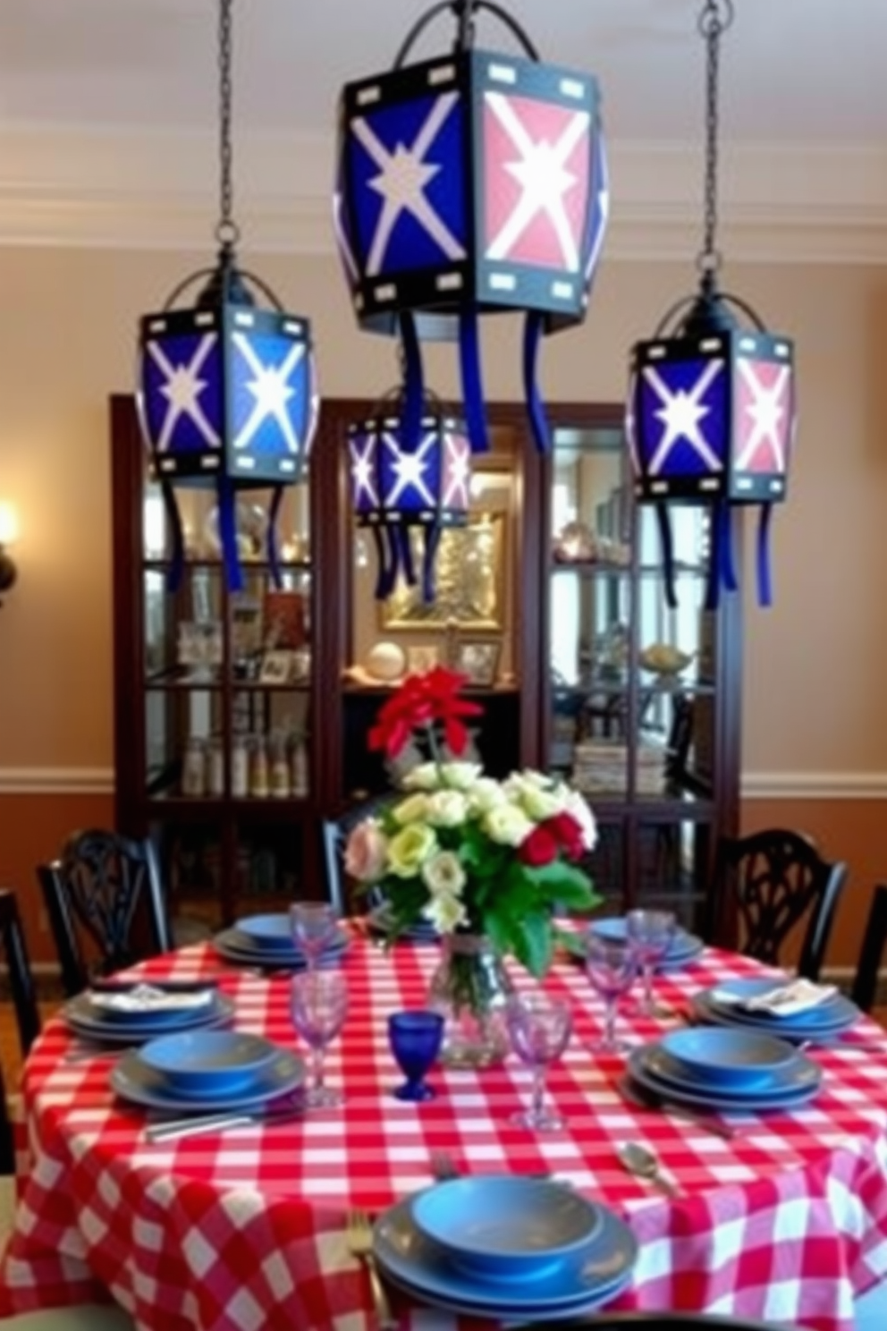 A festive dining room setting featuring decorative lanterns adorned with flag motifs hanging from the ceiling. The table is elegantly set with a red and white checkered tablecloth, complemented by blue dinnerware and fresh flowers in a vase at the center.