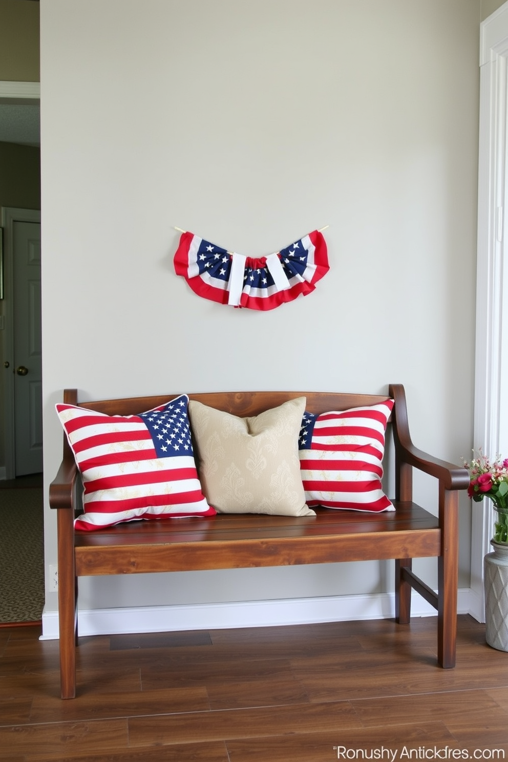 American flag throw pillows are arranged on a rustic wooden bench situated in a welcoming entryway. The space is adorned with patriotic decor, including a small American flag banner draped above the bench, creating a festive atmosphere for Memorial Day.