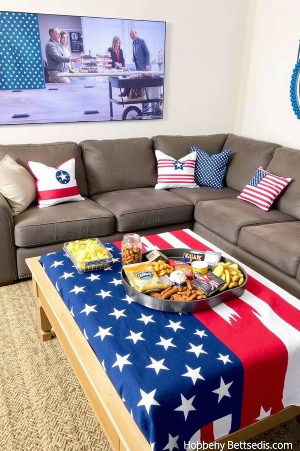 A cozy home theater setting decorated for Memorial Day features a large sectional sofa adorned with patriotic throw pillows. The coffee table is covered with an American flag tablecloth, upon which an array of snacks is artfully displayed.