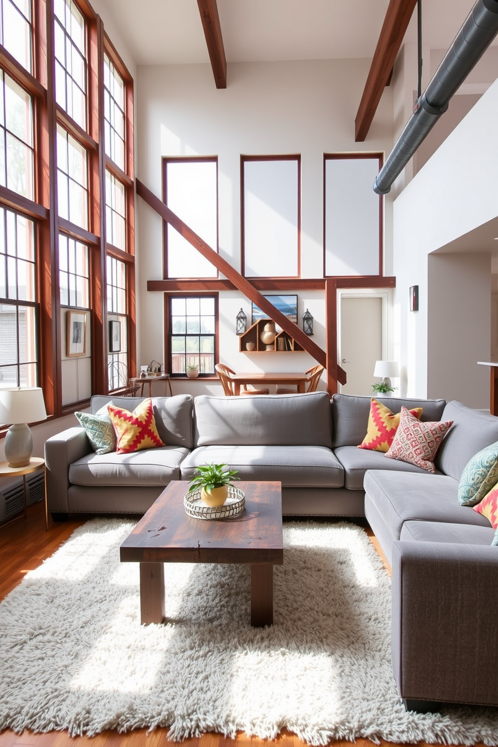 A cozy loft living room features a large comfortable sectional sofa in a soft gray fabric, adorned with colorful throw pillows for a touch of vibrancy. Natural light floods the space through large windows, highlighting a rustic wooden coffee table placed in front of the sofa and a plush area rug underneath.