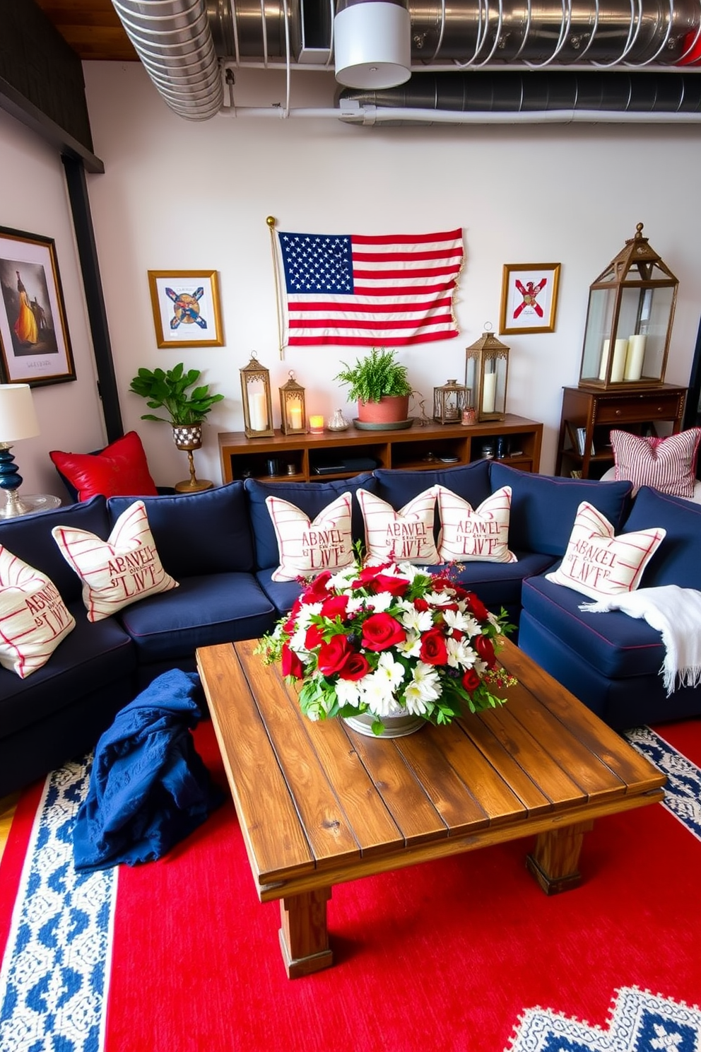 A stylish loft decorated for Memorial Day featuring a mix of red, white, and blue accents. The space includes a large sectional sofa in a deep navy hue paired with bright white throw pillows and a vibrant red area rug. On the walls, framed vintage American flags add a patriotic touch while decorative lanterns in varying heights provide warm lighting. A rustic wooden coffee table is adorned with a centerpiece of fresh flowers in red and white, creating a festive atmosphere.