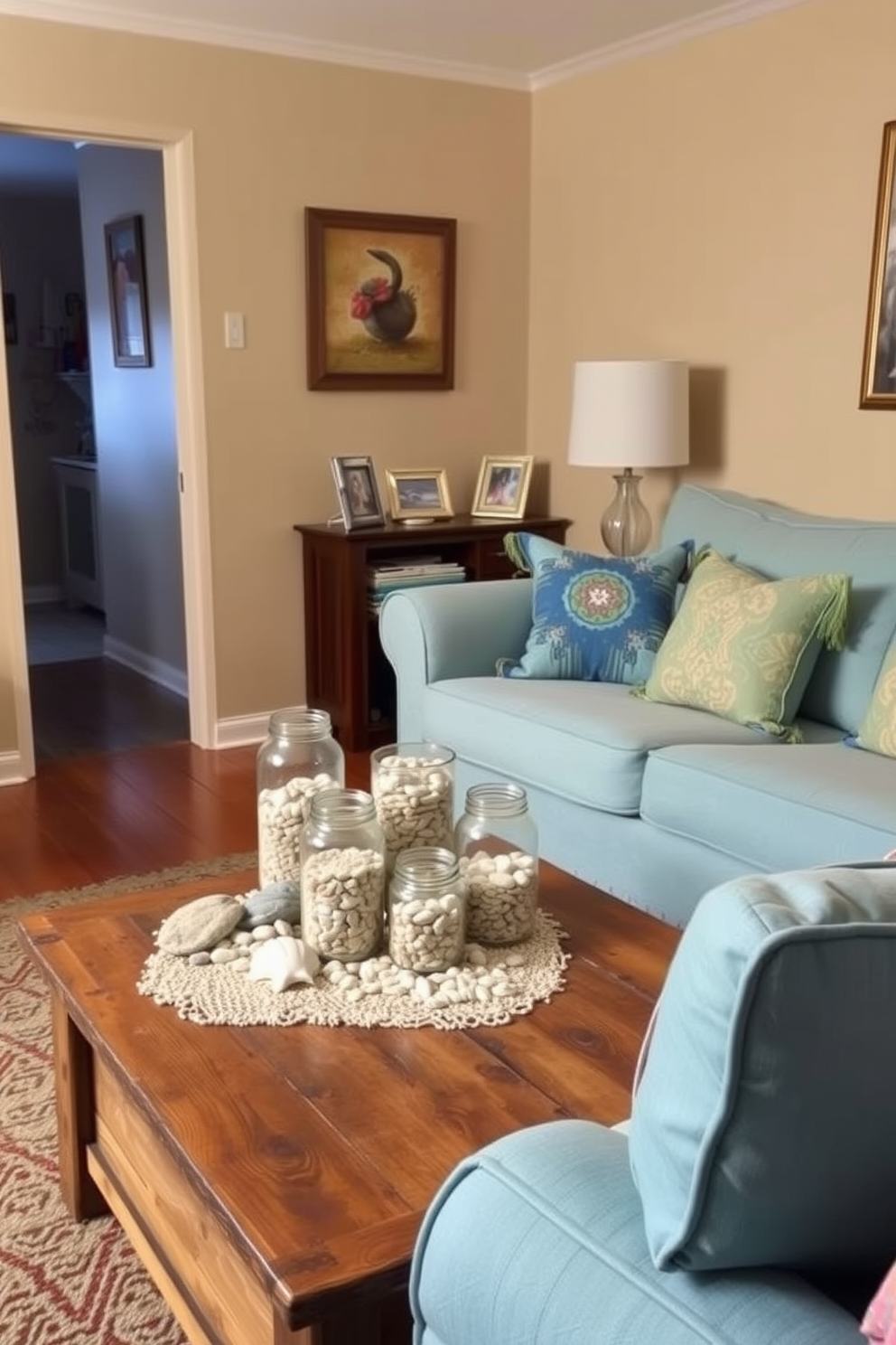 A cozy small living room featuring decorative jars filled with sand and shells arranged on a rustic wooden coffee table. The walls are painted in a soft beige, and a light blue couch with colorful throw pillows complements the beach-inspired decor.